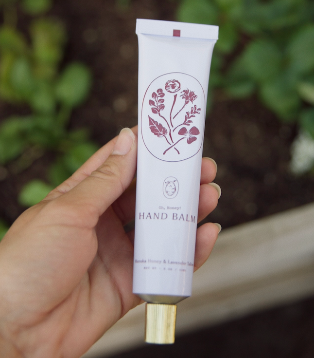 Hand holding a tube of hand balm with a floral design on a blurred natural background