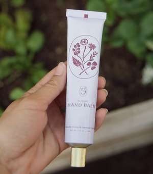 Hand holding a tube of hand balm with a floral design on a blurred natural background