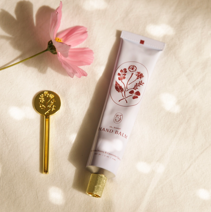 Hand holding a tube of hand balm with a floral design on a blurred natural background