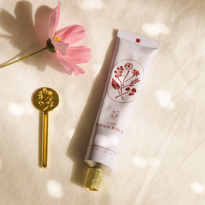 Hand balm with floral design on a textured surface with a pink flower and gold key.