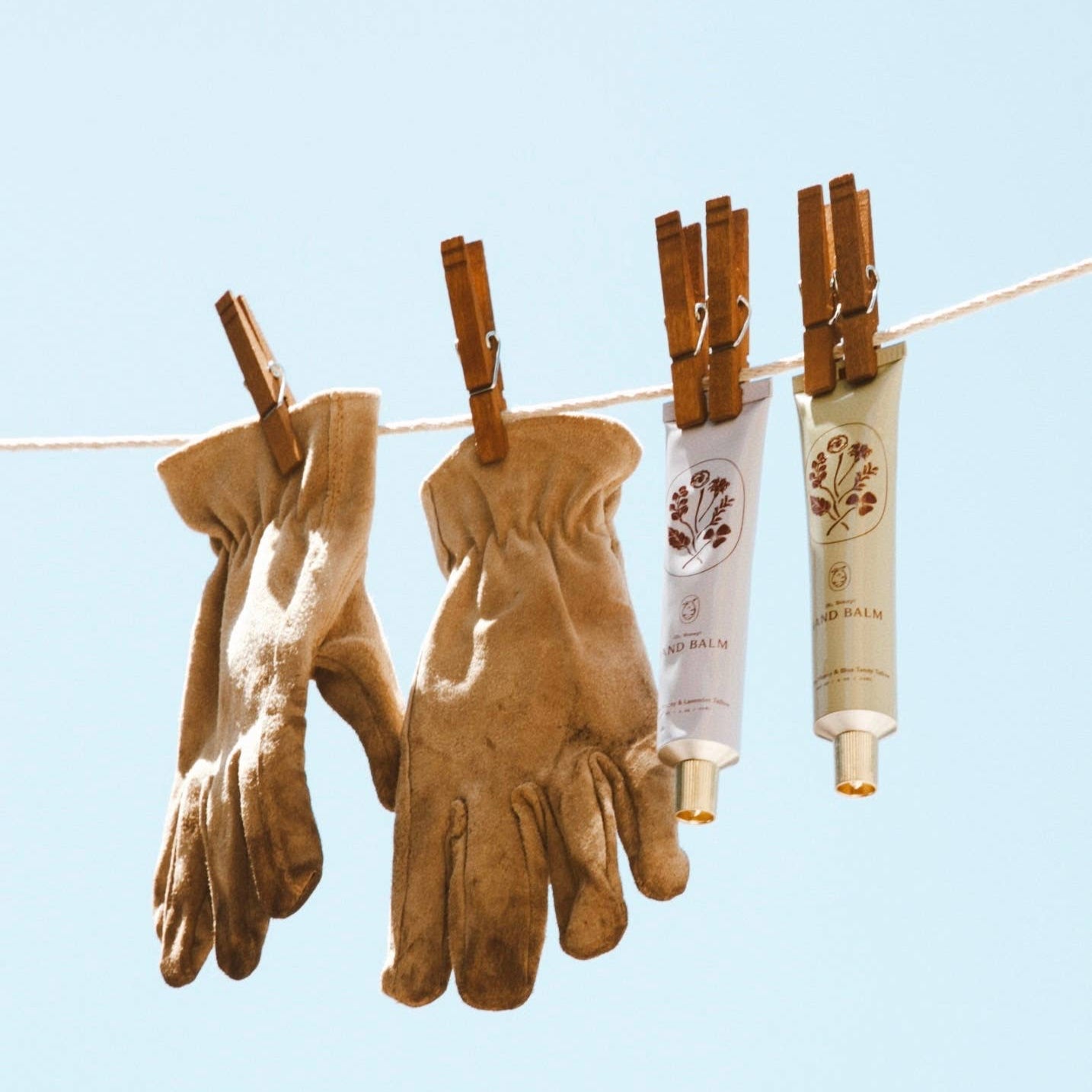 Brown gloves and two tubes of cream hanging on a clothesline against a light blue background