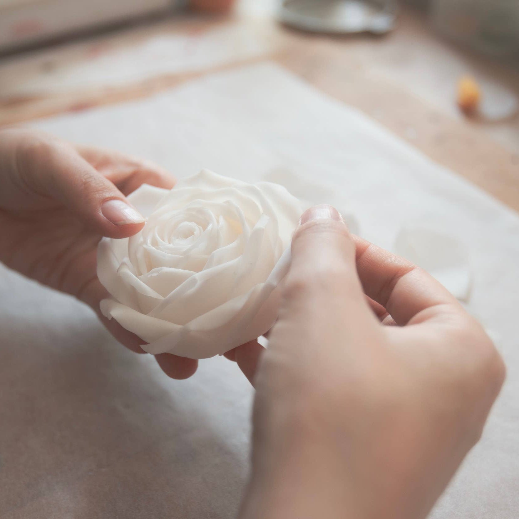Person holding a white flower-shaped object on a wooden surface