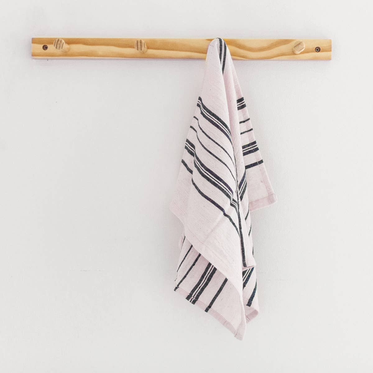 A striped cotton tea towel laid out on a surface, with black stripes on a cream background.