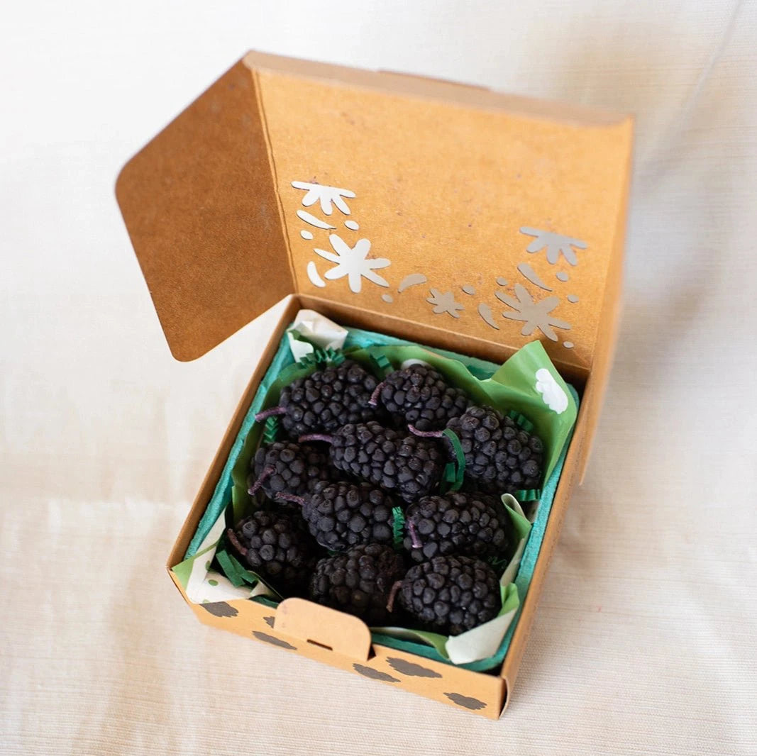 A box of Happy Organics Blackberry Beeswax Birthday Candles in a brown paper box on a light colored background. 