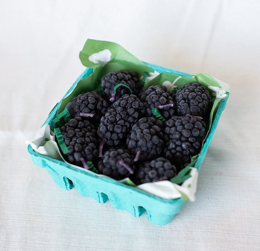 A box of Happy Organics Blackberry Beeswax Birthday Candles in a brown paper box on a light colored background. 