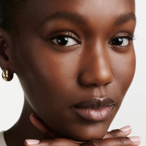 Close-up of a woman with a neutral expression and hands on her face against a white background
