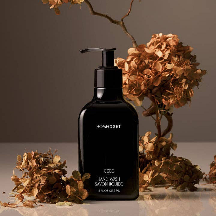 Black pump bottle labeled 'Homecourt' with dried flowers on a reflective surface.