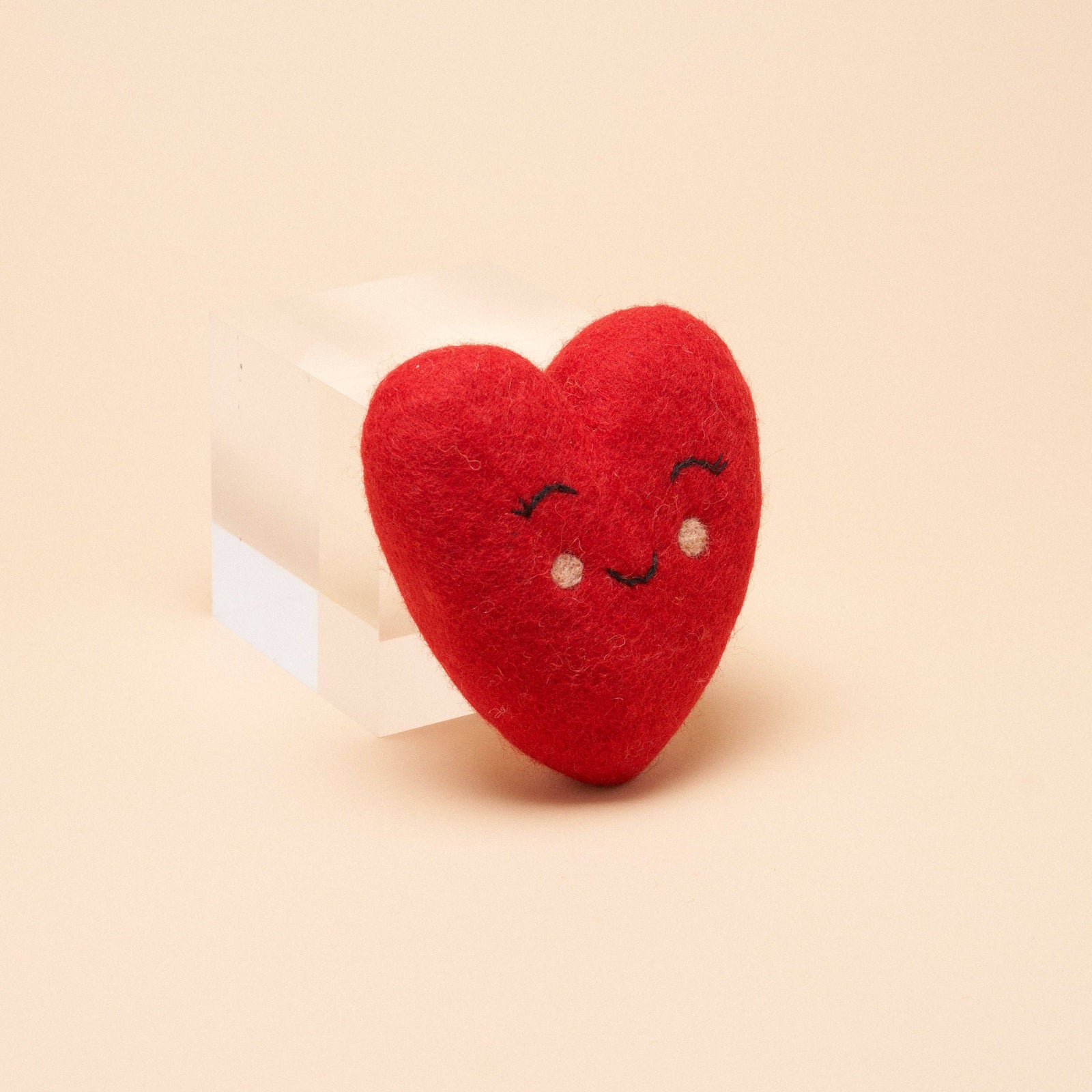 A red wool felt heart shaped dog toy, with a smile and eyes embroidered on it