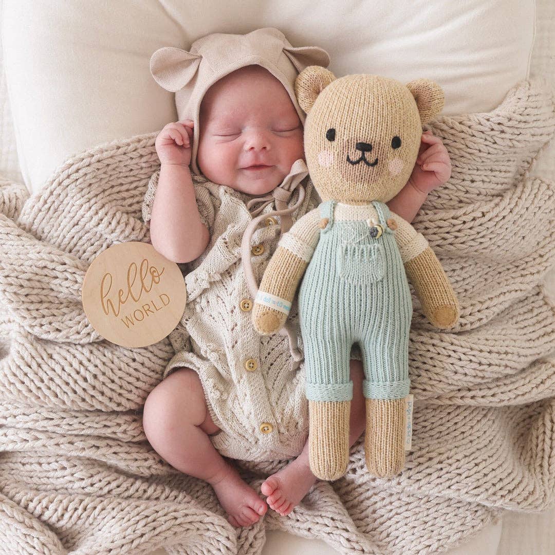 A baby on a beige bed with a honey bear stuffed animal