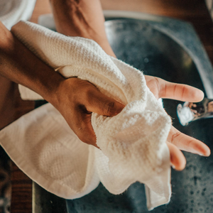 Person drying hands with a white towel in front of a sink.