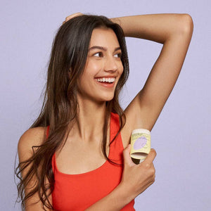 A woman with long dark hair and a red halter top applying hibar deodorant. 