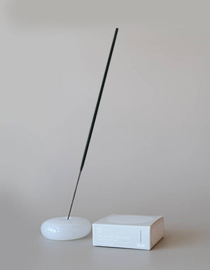 Incense stick on a white base with a white box against a plain background
