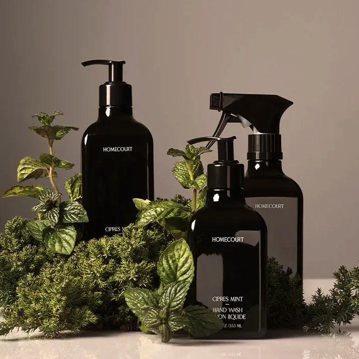 Three black Homecourt bottles with greenery on a neutral background