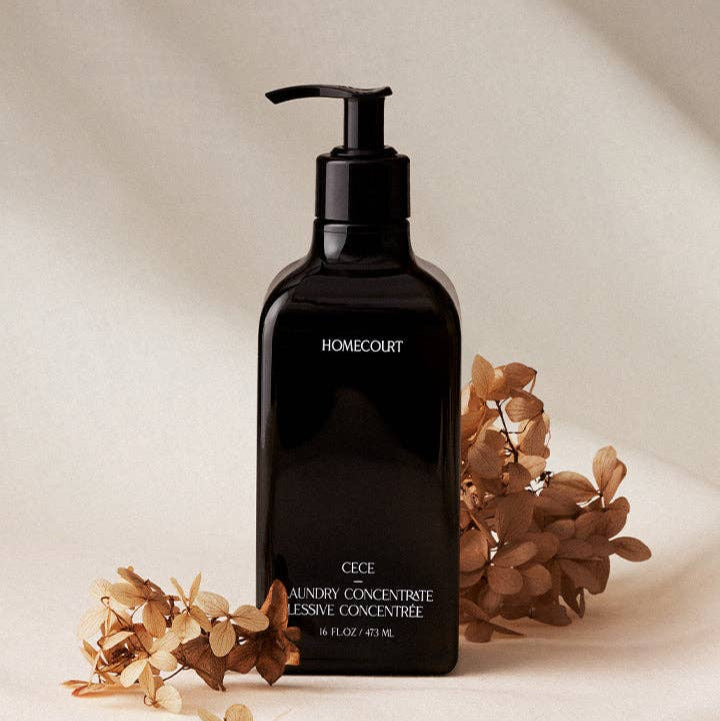 Black bottle of Homecourt laundry concentrate with dried flowers on a beige background