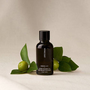 Black bottle of Homecraft Neroli Leaf fragrance oil with green leaves on a beige background