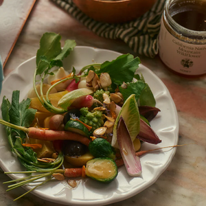 A plate of fresh vegetables next to a jar of Flamingo Estate California honey