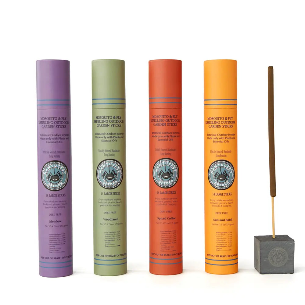 Four cylindrical incense sticks in different colors with a wooden stick and gray base on a white background.