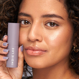 Woman holding a purple Indie Lee product close to her face