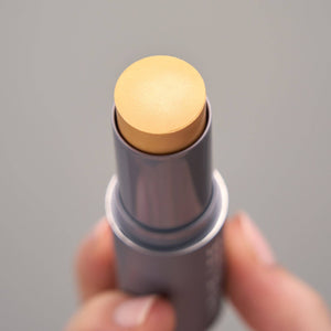 Hand holding a makeup stick with beige color on a gray background