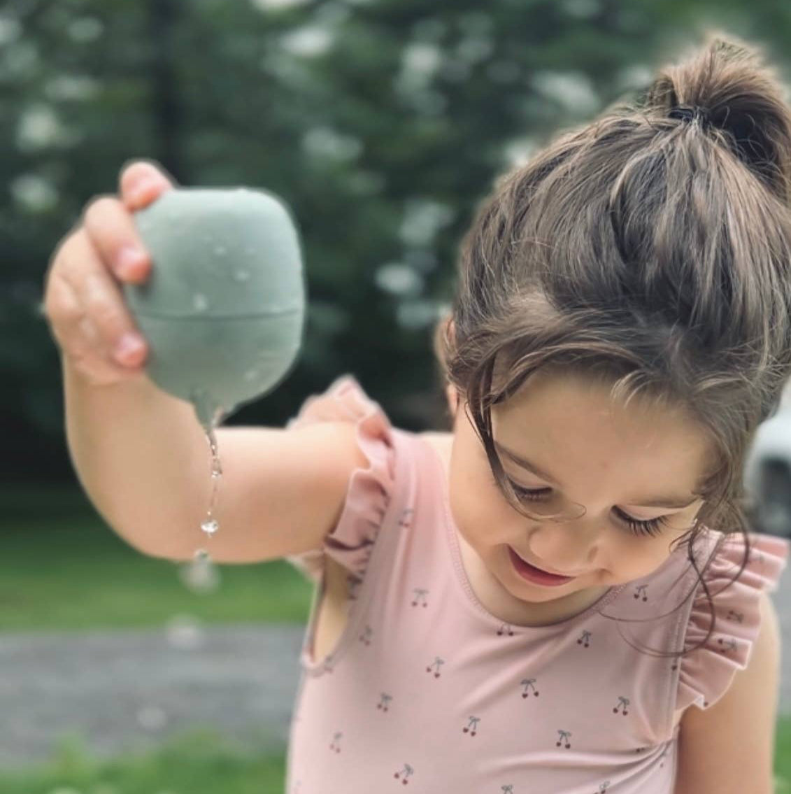 A little girl in a pink swimsuit plays with a Brooklyn neutral water toy. 