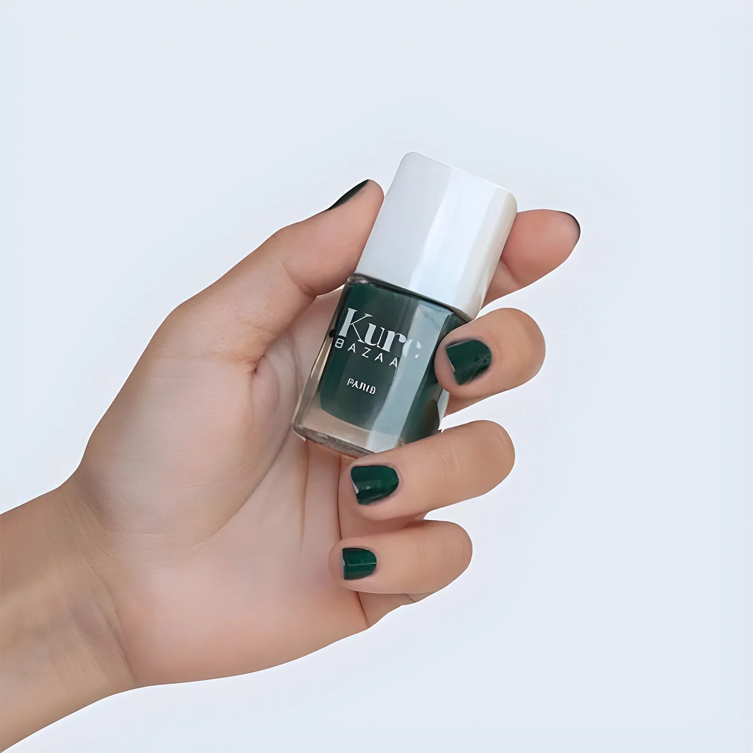 A person hiding a bottle of kure bazaar nail color in kale with green fingernails. 