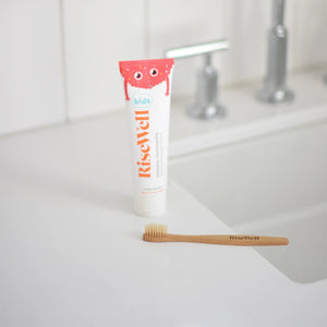 Tube of RiseWell toothpaste and a wooden toothbrush on a bathroom counter.