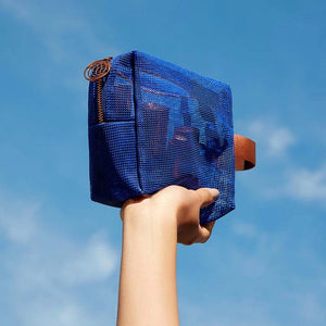 Hand holding a blue mesh pouch against a clear blue sky