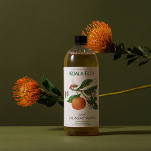A bottle of Koala Eco natural, organic laundry detergent with two orange flowers