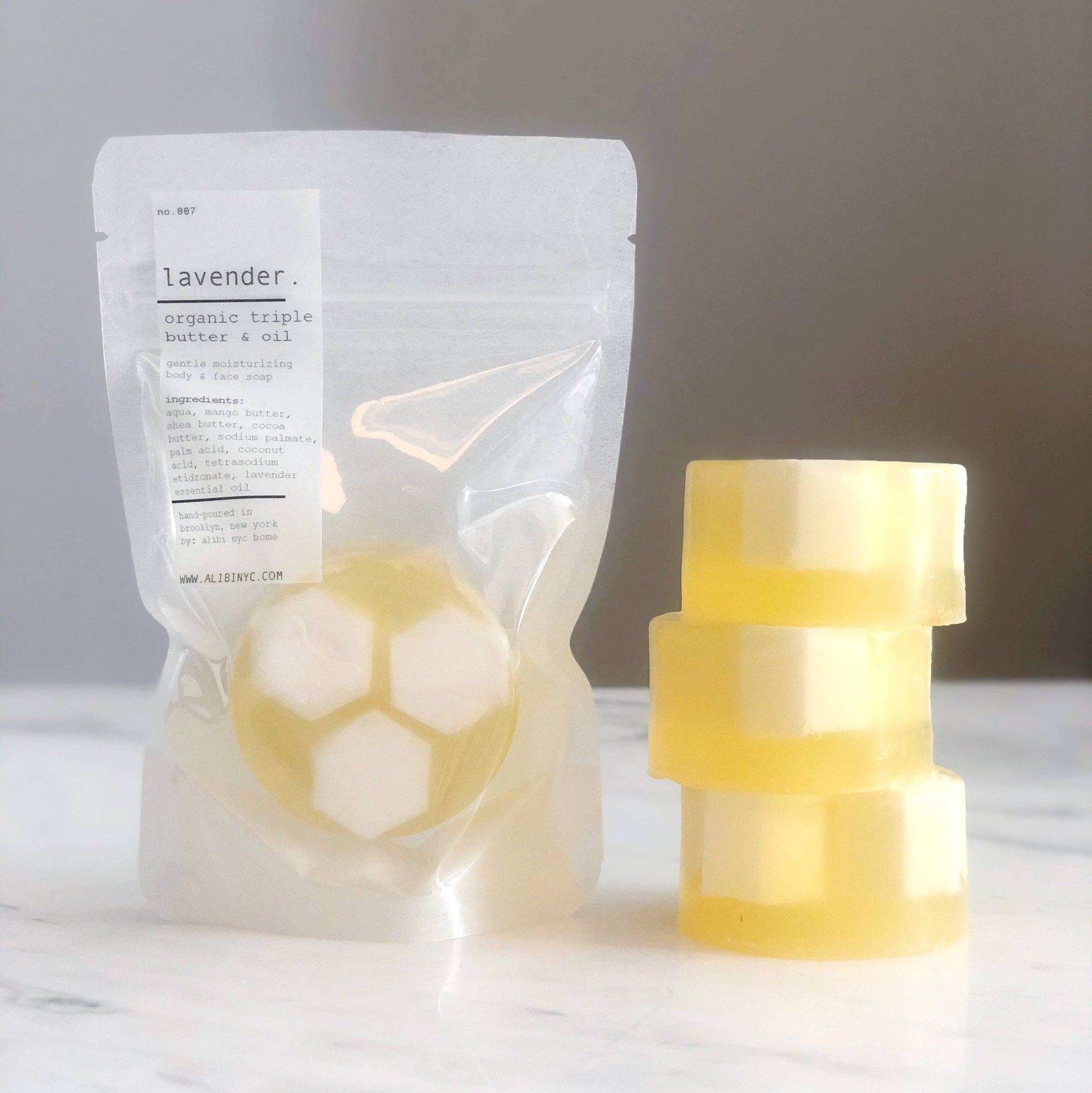 Two yellow soap bars with circular designs on a white surface, next to a clear plastic bag labeled 'Lavender'.