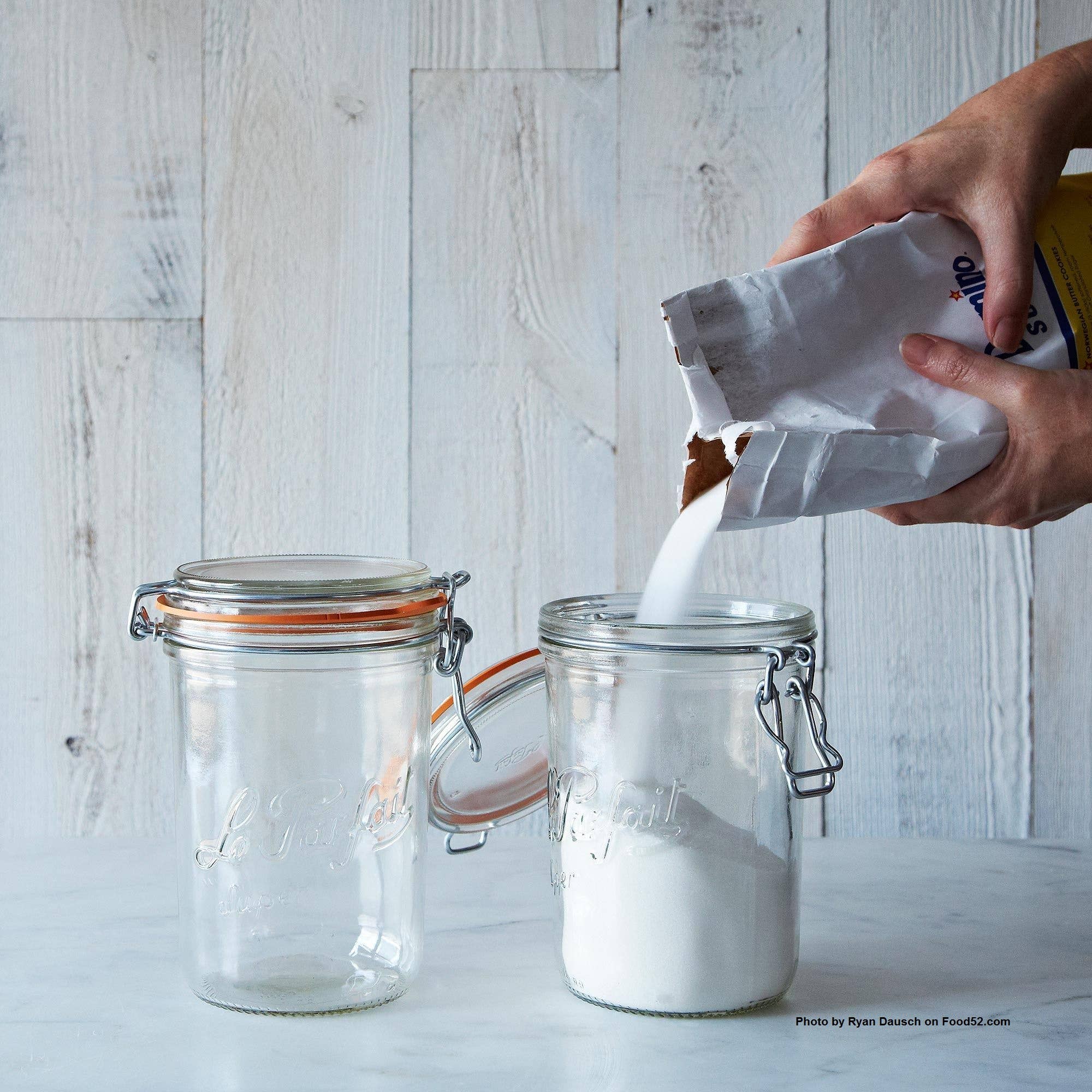 A person pouring a bag of sugar into a le parfait container. 