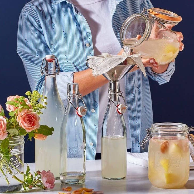 A person pouring lemonade into glass bottles. 