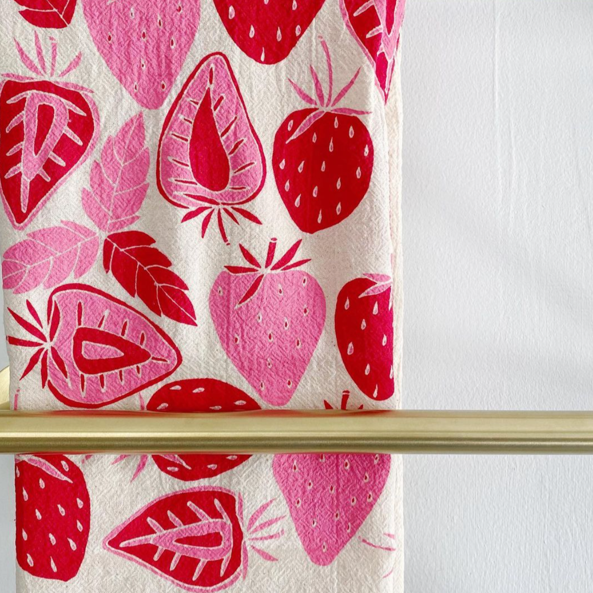 A strawberry printed tea towel on a gold bar. 