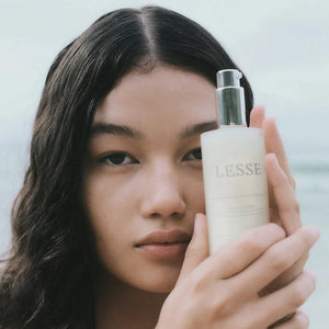A woman with long dark hair holds a bottle of Lesse calming cleanser