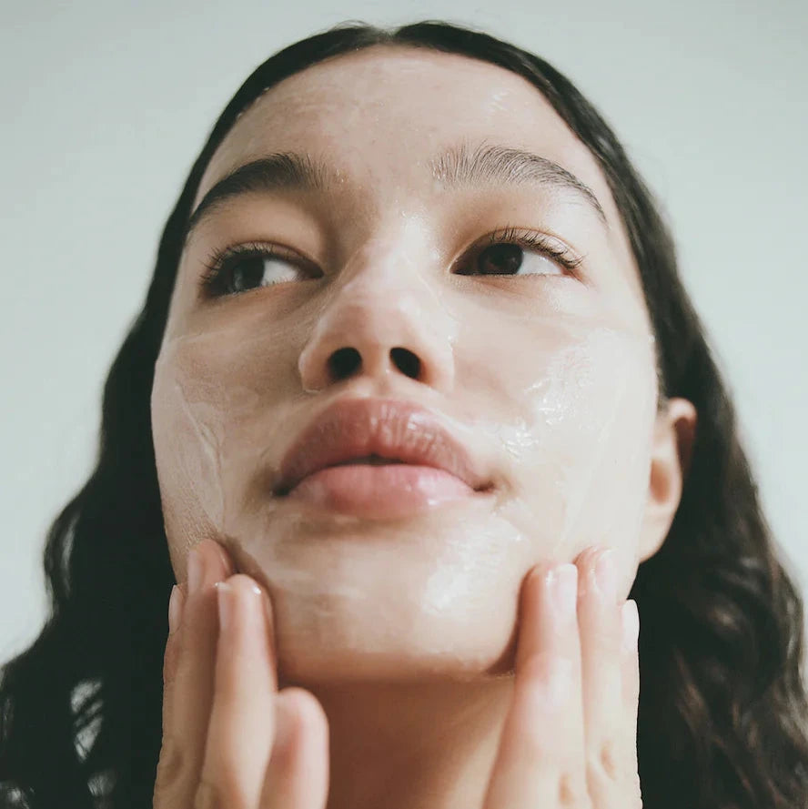 A woman with dark hair applies the Lesse calming cleanser to her face