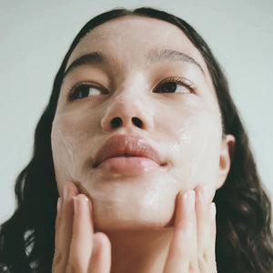 A woman with dark hair applies the Lesse calming cleanser to her face