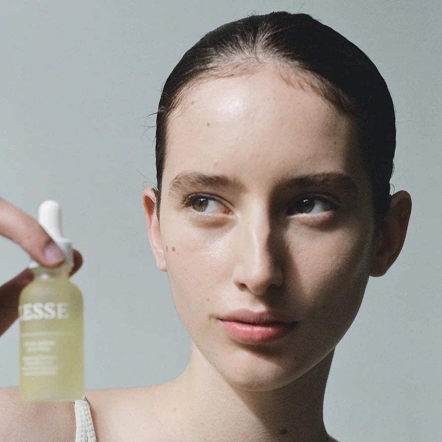 A woman with dark hair holding a bottle of Lesse ritual serum
