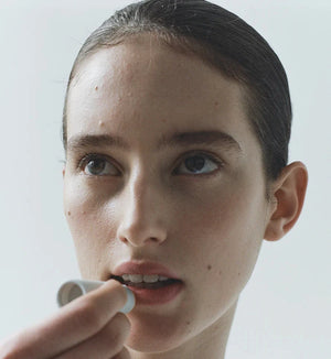 A person applying Lesse soothing lip balm to their lips