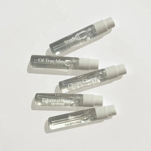 Five clear vials of perfume with white tops on a white background. 