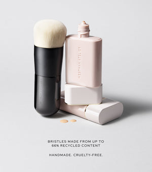 Makeup brush and foundation bottle with text about recycled bristles on a light gray background