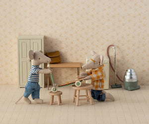 Two toy mice in a room with furniture and cleaning equipment.