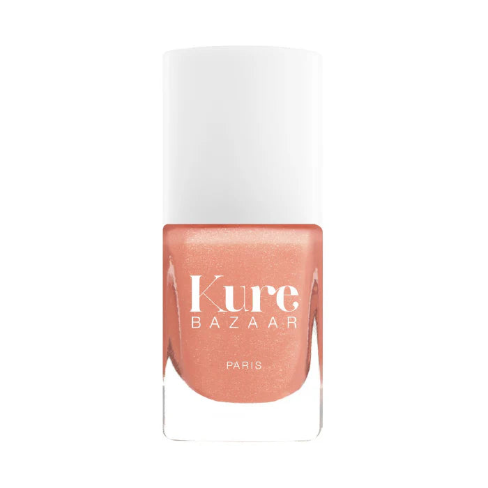 A bottle of Kure Bazaar nail polish in a peachy coral color with a translucent finish, labeled in Paris.