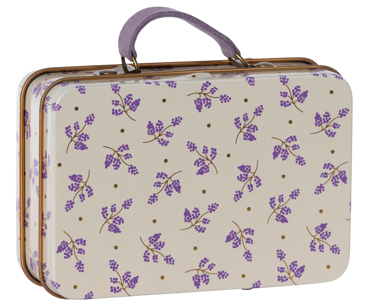 A small metal suitcase with a lavender floral pattern on a cream background, with a purple handle.