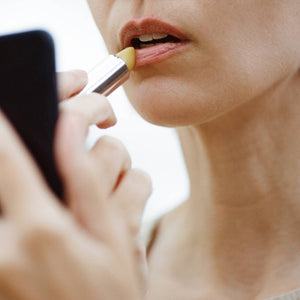 Person applying makeup with a brush to their lips, using a mirror.