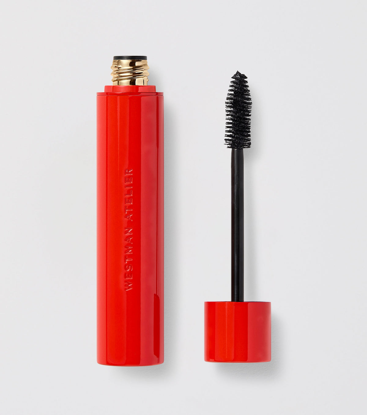 A red mascara tube with the cap off, showing the wand with bristles coated in black mascara.