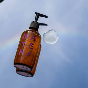A bottle of Mater hand and body soap on a mirror with grass in the background. 