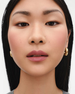 Close-up of a person with dark hair and gold earrings on a white background