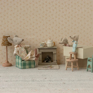 Miniature diorama with toy mice and furniture against a patterned wall.