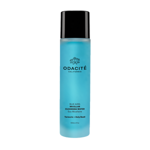 A blue bottle of Odacite Blue Aura Micellar Cleansing Water with white and black text, and a floral design near the cap.