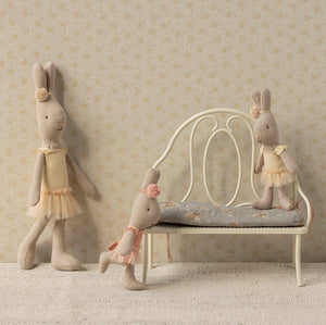 Three stuffed rabbit toys in a child's room setting with a small bed and chair.