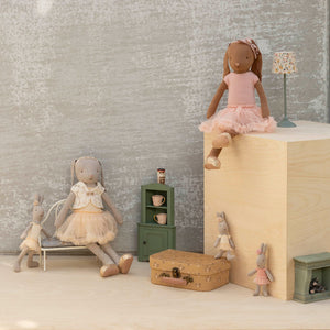 Toy dolls and accessories arranged in a room setting with a textured wall.